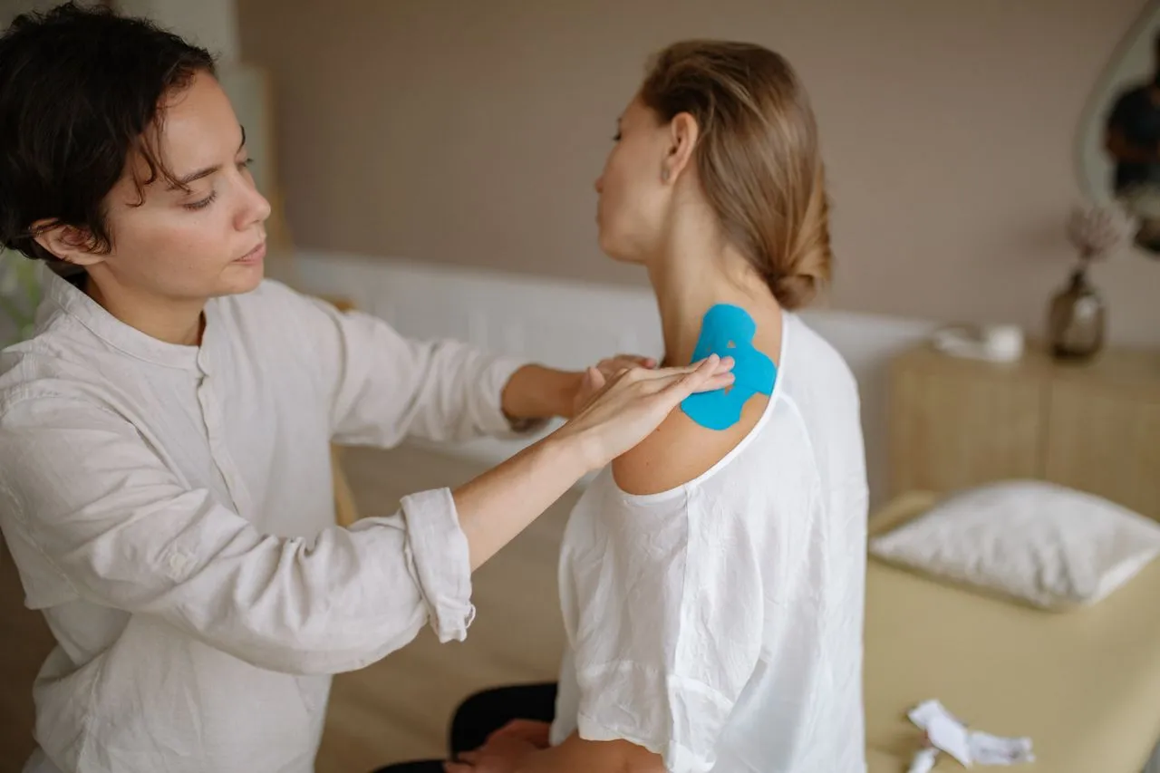 Therapist applying kinesiology tape to a patient’s shoulder